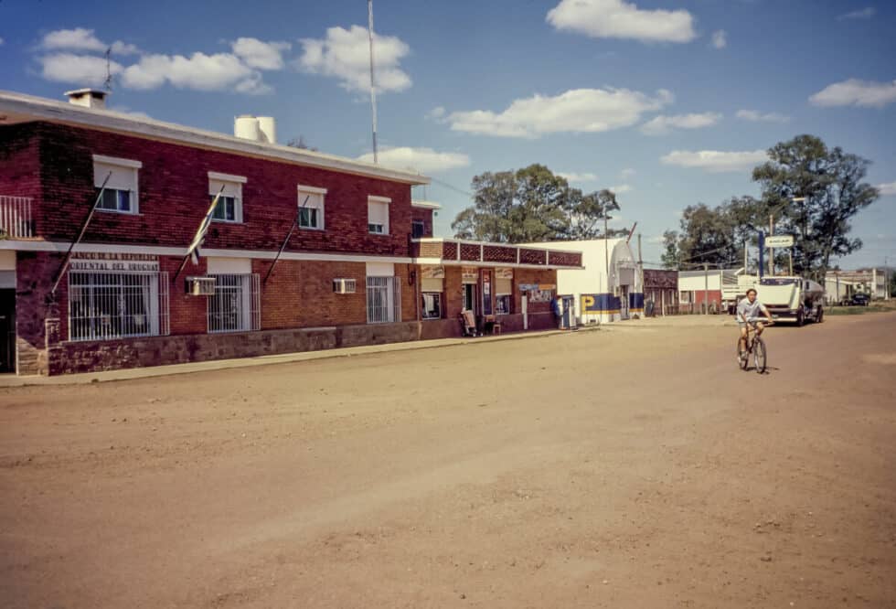 Main street Baltasar Brum with bank on corner and one boy on a bike in the road. A Peace Corps volunteer’s story in Baltasar Brum, Uruguay.