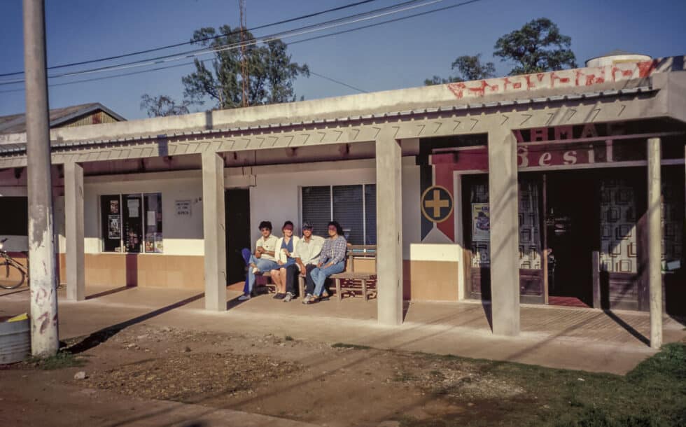 Pharmacy and four people sitting on a bench waiting for the bus. A Peace Corps volunteer’s story in Baltasar Brum, Uruguay.