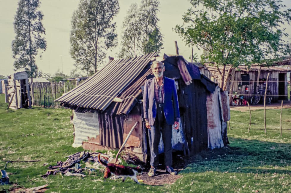 Man standing in front of his home no bigger than a shed made of corrugated tin. A Peace Corps volunteer’s story in Baltasar Brum, Uruguay.