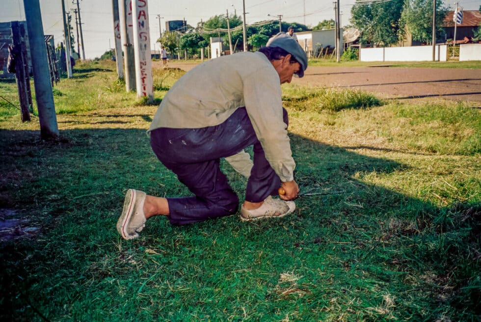 Kneeling and cutting the grass with hedge clippers. A Peace Corps volunteer’s story in Baltasar Brum, Uruguay.
